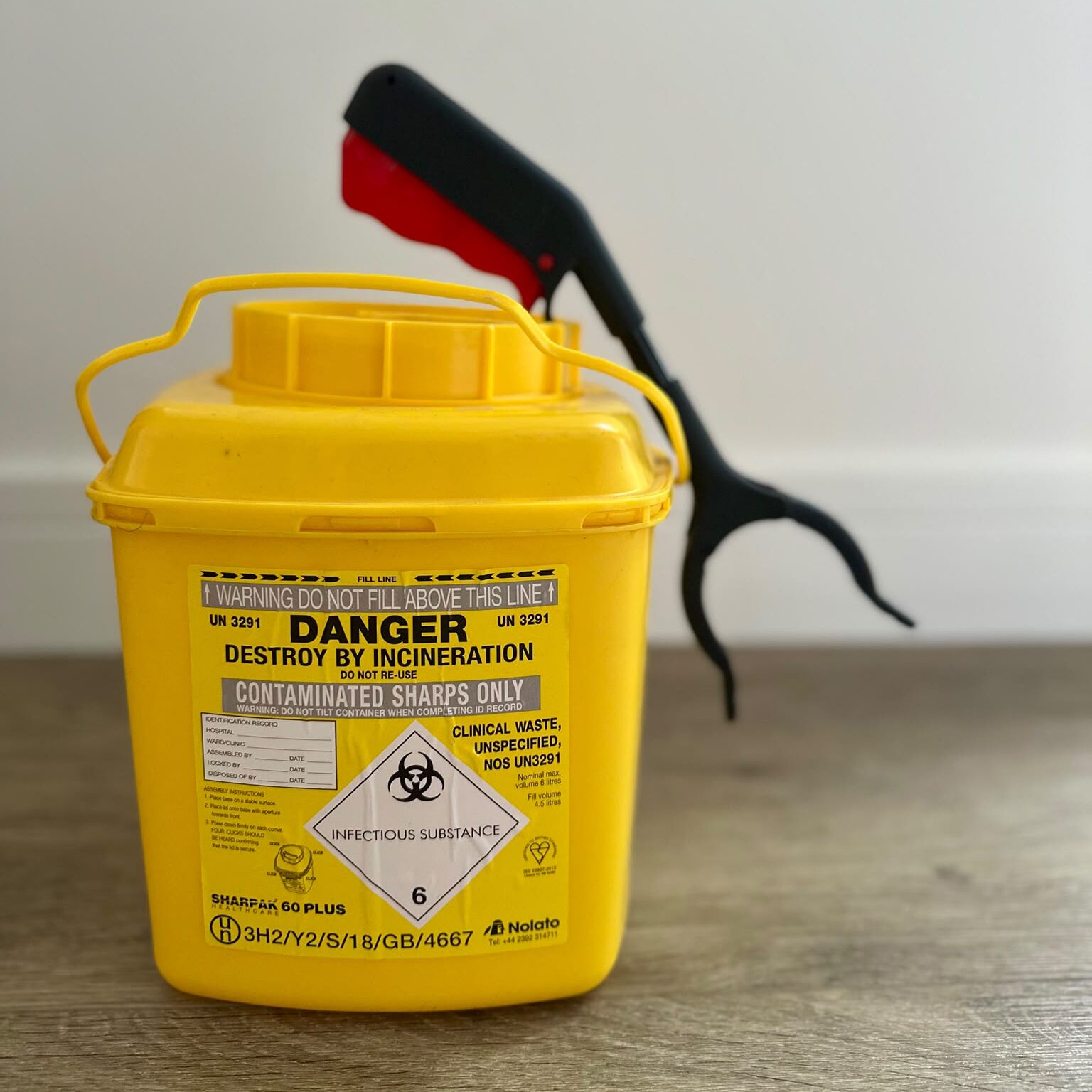 A sharps removal yellow waste bucket and grabber which is used to safely dispose of hazardous waste